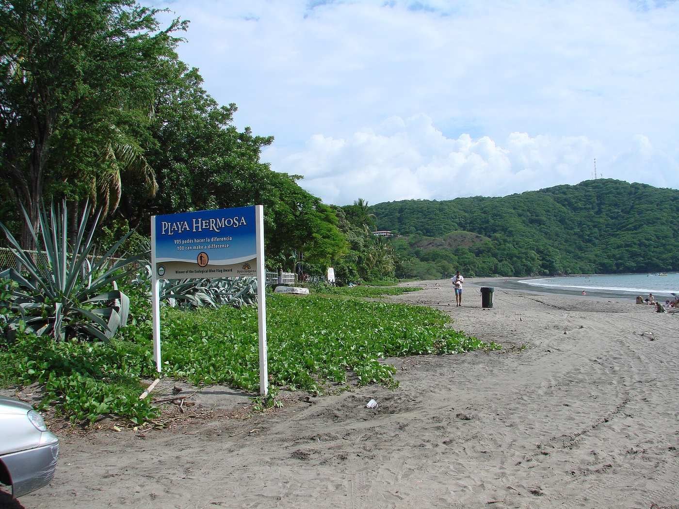 The sign at the entrance to Playa Hermosa with the long grey sand beach behind
