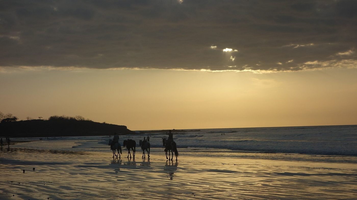 Riders on horseback along the wet sand at Tamarindo at sunset