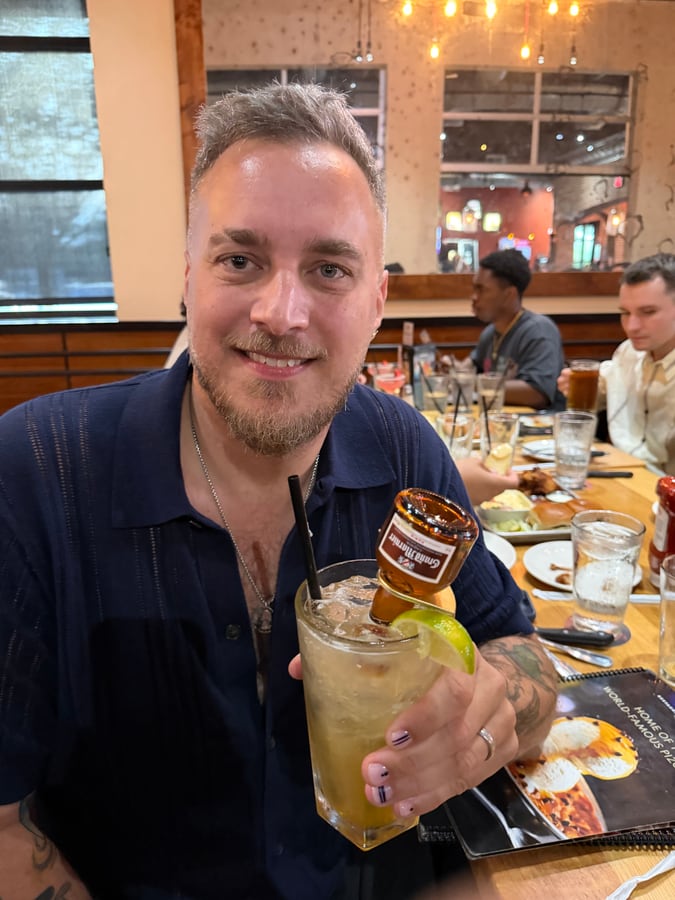 Holding up a tall cocktail with a beer bottle upended in it at a restaurant table