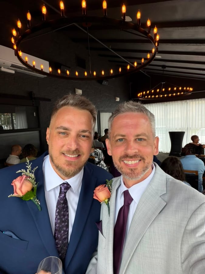 The two of us in suits with rose boutonnieres at a wedding